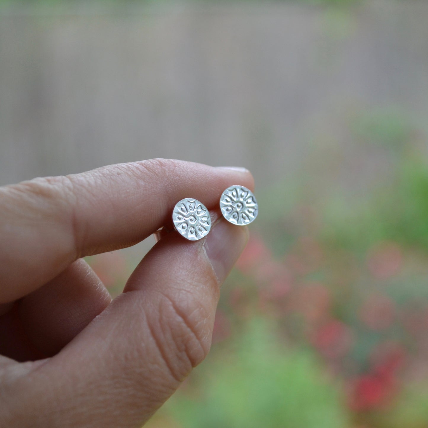 silver post earrings flower design held in hand